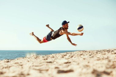 Spor kıyafetlerine odaklanmış, deniz kenarında voleybol oynayan, Jumbo oynayan ve kuma düşen spor, yaz, doğa, aktif yaşam tarzı, gençlik.