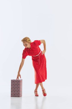 Canlı kırmızı benekli bir elbise giyen bir kadın, beyaz arka planda izole edilmiş bir hediyeyle poz veriyor. Tatil ruhu. Eski moda kavramı, kutlama, parti, hazırlık