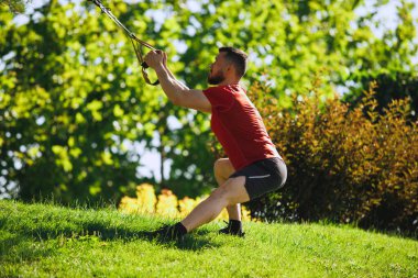 Spor kıyafetleri içinde spor kıyafetleri içinde spor kaslı atletik bir adam açık havada yeşillik parkına karşı trans fitness bantları takıyor. Spor, vücut ve sağlık anlayışı, aktif yaşam tarzı