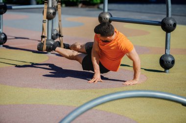 Atletik erkek spor giyim kuşaklarına ayak basıyor, tahta egzersizleri yapıyor, güç kazanıyor. Açık hava traks egzersizi. Spor, vücut ve sağlık anlayışı, aktif yaşam tarzı, dayanıklılık