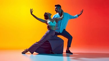 Zarif bir hareket. Tarz sahibi genç bir çift, erkek ve kadın dans eden bachata, neon ışıkta sarı renkli arka planda performans sergiliyorlar. Dans, performans, sanat, eğlence kavramı