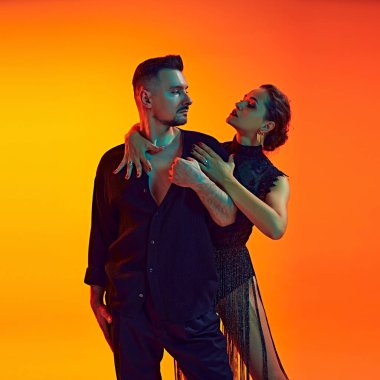 Yakışıklı bir erkek ve güzel bir kadının portresi, tutkulu bir çift neon ışıkta sarı renkli arka planda dans ediyor. Dans, performans, sanat, eğlence kavramı