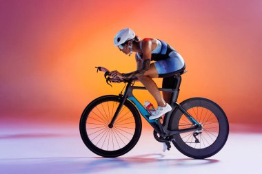 Renkli spor giyim ve beyaz kasklı bisiklet süren bisikletçi. Neon ışıkta turuncu ve pembe arka planda. Spor, rekabet, turnuva, şampiyonluk, hız, dayanıklılık kavramı