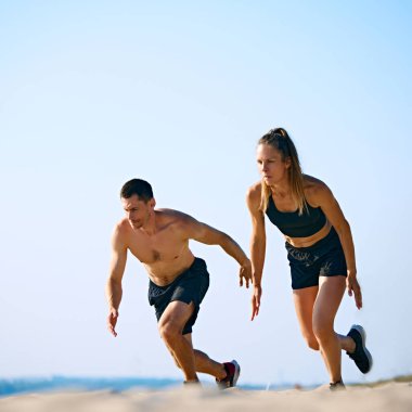 Dinamik ve sıkı antrenman açık havada. Kumsalda antrenman yapan genç bir adam ve bir kadın, açık gökyüzünün altında koşuyorlar. Spor anlayışı, aktif ve sağlıklı yaşam tarzı, vücut bakımı, fitness