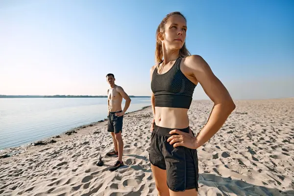 Siyah spor kıyafetleriyle nehir kıyısında spor kıyafetleri giymiş, fit vücutlu bir kadın ve erkek. Açık hava antrenmanı. Spor anlayışı, aktif ve sağlıklı yaşam tarzı, vücut bakımı, fitness