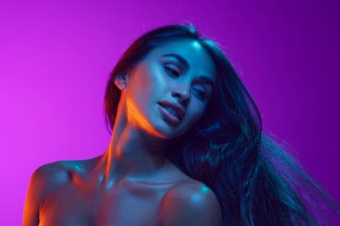 Duygusallık ve kadınlık. Çekici, sağlıklı bir cilde ve parlak saçlara sahip genç bir kadın neon ışıkta mor arka plana karşı. Güzellik, cilt ve vücut bakımı, kozmetik ve kozmetik kavramı