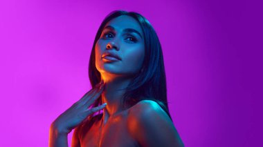 Kadınlık ve duygusallık. Çıplak omuzlu çekici zarif genç kadınlar, uzun siyah saçlar, neon ışıkta mor arka plana karşı. Güzellik, cilt ve vücut bakımı, kozmetik ve kozmetik kavramı