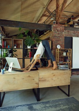 Resmi giyinmiş bir kadın bilgisayar ve ofis malzemelerinin yanında duruyor ve esneme egzersizleri yapıyor. İş ve sağlığın karışımı. İş hayatı kavramı, iş ve spor arasındaki denge