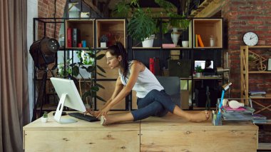 Odaklanmış bir kadın, resmi bir çalışan yoga pozisyonunda masa başında oturmuş bilgisayar başında çalışıyor. Harmanlama görevleri ve sağlıklı egzersizler. İş hayatı kavramı, iş ve spor arasındaki denge, iş