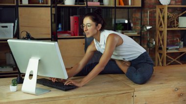 Kadın, resmi giyinen ve gözlüklü bir çalışan, yoga pozisyonunda oturan ve bilgisayarla odaklanan, modern ofis hayatı tarzında çalışan. İş hayatı kavramı, iş ve spor arasındaki denge, iş