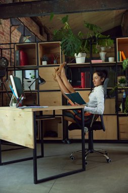 Kadın, modern ofisin çalışanı, esneme egzersizleri yaparken bilgisayarla çalışıyor. Çağdaş çalışma alanında fiziksel aktivite ve verimlilik. İş ve spor arasındaki denge kavramı