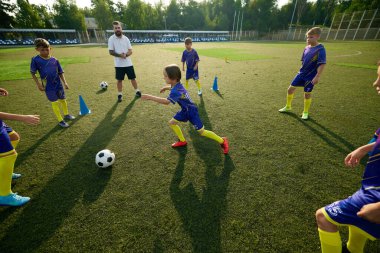 Çocuk, çocuk, futbol oyuncusu sahada top sürüyor, koç ise eğitim ve destek sağlıyor. Açık hava futbol maçı. Spor, çocukluk, eğitim, başarı, aktif yaşam tarzı kavramı