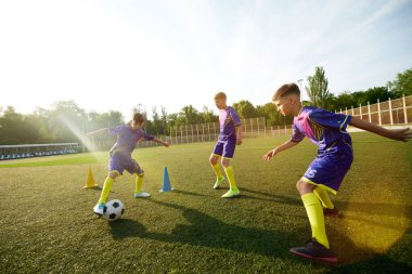 Küçük aktif çocuklar, spor giyimli çocuklar güneşli bir günde açık hava stadyumunda antrenman yapıyorlar. Futbol becerileri ve takım ruhu gelişiyor. Spor, çocukluk, eğitim, başarı, aktif yaşam tarzı kavramı