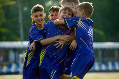 Zaferin dinamik anı. Çocuklar, mavi üniformalı arkadaşlar, hareket halindeki futbolcular, zıplamak ve sarılmak, galibiyeti kutlamak. Spor, çocukluk, eğitim, başarı, aktif yaşam tarzı kavramı