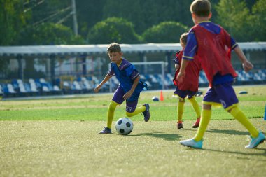 Çocuklar, kırmızı ve mavi üniformalı çocuklar açık hava stadyumunda, zafer için yarışıyorlar, futbol antrenmanı yapıyorlar. Spor, çocukluk, eğitim, başarı, aktif yaşam tarzı kavramı