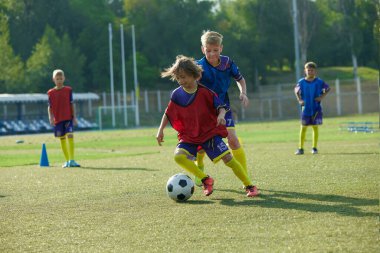 Genç oyuncular tekniklerini geliştirir, kırmızı ve mavi üniformalı çocuklar, futbol oyuncuları açık hava stadyum eğitiminde hareket halindedir. Spor, çocukluk, eğitim, başarı, aktif yaşam tarzı kavramı