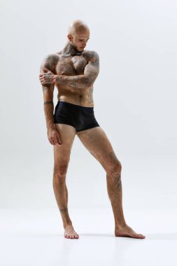 Uzun boylu, kaslı, üstsüz, dövmeleri olmayan beyaz stüdyo arka planında iç çamaşırlarıyla poz veren yakışıklı bir genç. Erkek güzelliği, vücut ve sağlık hizmetleri, spor