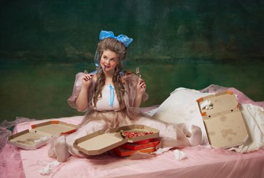 Çekici bir genç kadın portresi, lüks elbiseli prenses tatmin olmuş bir yüzle yatakta oturuyor ve kaliteli yeşil arka planda lezzetli pizzalar yiyor. Tarih kavramı, çağların karşılaştırması