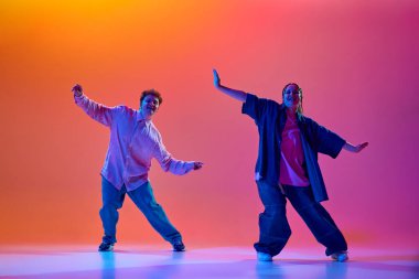 Genç bir adam ve kadının dinamik görüntüsü, günlük kıyafetleriyle neon ışıklarıyla hip-hop dansı yapıyor. Çağdaş dans, hobi, gençlik kavramı