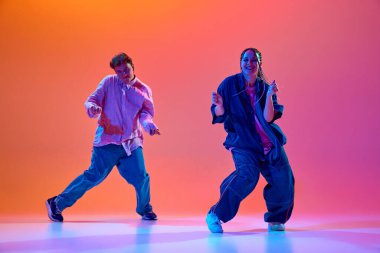 Modern dans stillerinin enerjisi. Genç insanlar, tutkulu erkek ve kadın, neon ışıklarıyla hip-hop dansı yapan gradient stüdyo arkaplanı. Çağdaş dans, hobi, gençlik kavramı