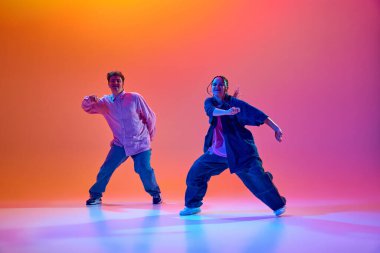 Genç bir adam ve kadının dinamik görüntüsü, günlük kıyafetleriyle neon ışıklarıyla hip-hop dansı yapıyor. Çağdaş dans, hobi, gençlik kavramı