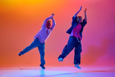 Modern dans stillerinin enerjisi. Genç insanlar, tutkulu erkek ve kadın, neon ışıklarıyla hip-hop dansı yapan gradient stüdyo arkaplanı. Çağdaş dans, hobi, gençlik kavramı