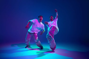 Enerji patlaması. Sanatçı genç sanatçılar, erkek ve kadın hip-hop dansçıları, neon ışıkta mor stüdyo arka planına karşı modern dans becerilerini gösteriyorlar. Çağdaş dans, hobi, gençlik kavramı