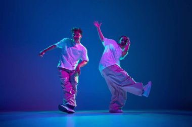 Esnek ve enerjik gençler, erkek ve kadın hip-hop dansçısı, neon ışıkta mor stüdyo arka planına karşı tutkuyla şarkı söylüyorlar. Çağdaş dans, hobi, gençlik kavramı