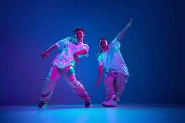 Esnek ve enerjik gençler, erkek ve kadın hip-hop dansçısı, neon ışıkta mor stüdyo arka planına karşı tutkuyla şarkı söylüyorlar. Çağdaş dans, hobi, gençlik kavramı