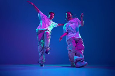Sanatsal ve enerjik genç erkek ve kadının dinamik görüntüsü, dansçılar neon ışıkta mor stüdyonun arka planına karşı hip-hop yapıyorlar. Çağdaş dans, hobi, gençlik kavramı