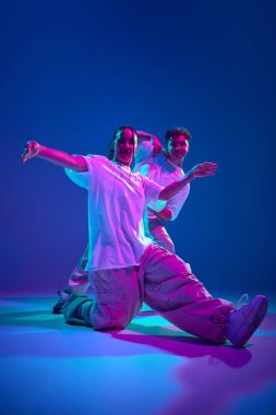 Sanatsal ve enerjik genç erkek ve kadının dinamik görüntüsü, dansçılar neon ışıkta mor stüdyonun arka planına karşı hip-hop yapıyorlar. Çağdaş dans, hobi, gençlik kavramı