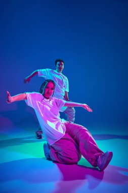 Sanatçı gençliği. Yetenekli genç kız ve erkeğin dinamik görüntüsü, hareket halindeki hip-hop dansçıları, neon ışıkta mor stüdyo arka planında performans sergiliyorlar. Çağdaş dans, hobi, gençlik kavramı