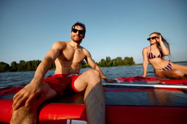 Genç insanlar, mayo ve güneş gözlüklü kadın ve erkek güneşli bir günde yemek masalarında dinleniyorlar. Kürek çekme aktivitesi. Spor anlayışı, yaz, aktif yaşam tarzı, hobi, boş zaman