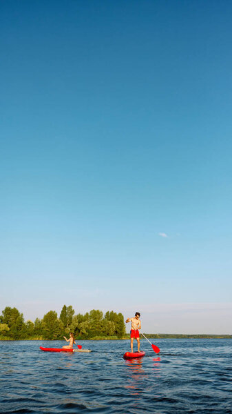 On the water activity. Young man and woman standing on sub boards with paddles, couple paddle boarding together, exploring river on bright day. Concept of sport, summer, active lifestyle, leisure time — Stock Image Water Activity Young Man Woman Standing Sub Boards Paddles Couple Stock Picture