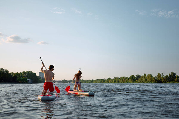 Young active people having dynamic evening, enjoying summer time on river while paddle boarding on sup boards. Concept of sport, summer, active lifestyle, hobby, leisure time — Stock Image Young Active People Having Dynamic Evening Enjoying Summer Time River Royalty Free Stock Photos