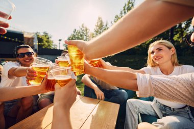 Bira bardaklarını tokuşturan insan ellerine odaklan. Arkadaşlar festival sırasında dışarıda buluşur, eğlenir, eğlenceli sohbetler ederler. Yaz kavramı, eğlence, arkadaşlık, toplantı, eğlence, rahatlama.