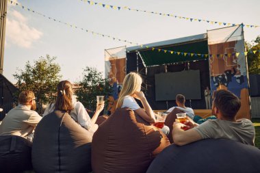 Müzik festivali, bir grup insan, erkek ve kadın, sıcak yaz gününde dışarıda toplanan arkadaşlar, bira içmek, konser izlemek. Yaz kavramı, eğlence, arkadaşlık, toplantı, eğlence, rahatlama.