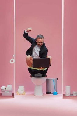 Duygusal iş adamı dizüstü bilgisayarla tuvaletin tepesinde oturmuş, canlı maç seyrediyor, pembe arka planda favori futbol takımını alkışlıyor. Spor, oyun, maç etkinliği, insan duyguları kavramı