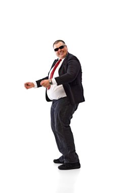 Dinamik ara veriyoruz. Siyah takım elbiseli şişman bir adam, beyaz gömlek ve güneş gözlüğü, çalışan dansı, beyaz arka planda izole edilmiş rahatlatıcı. İş anlayışı, eğlence, başarı.