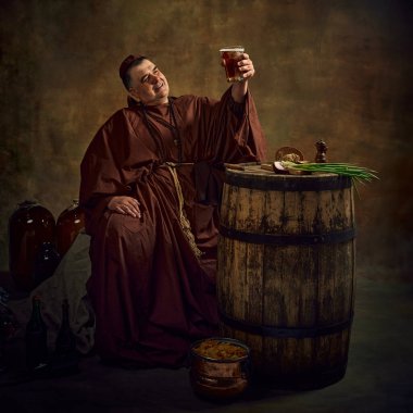 Ortaçağ keşişi, adam koyu renkli arka planda bira şişesi kaldırıyor. Huzurlu manastır ortamında demlenen eski bir manastır sanatı. Devir, tarih, bira fabrikası, gelenek karşılaştırması kavramı