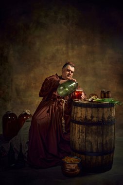 Bornozlu bir adam, keşiş bira dolduruyor, büyük şişeden bira içiyor ve esmer bir arka planı var. Manastır mayalamalarının tarihi gelenekleri. Devir, tarih, bira fabrikası, Ekim Festivali karşılaştırması kavramı