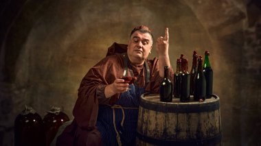 Reflecting centuries of monastic brewing. Medieval monk in traditional attire holding glass with drink, leaning on wooden barrel with various bottles. Concept of comparison of eras, history, tradition clipart