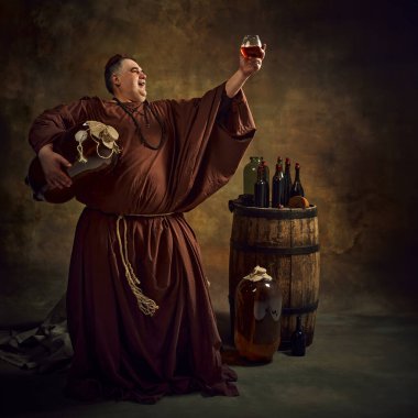 Proud man, medieval monk raising glass of ale, or cognac against vintage background with wooden barrel and bottles on top. Festival drinks. Concept of comparison of eras, history, brewery, traditions clipart