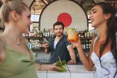 Erkeğe odaklan, barmen iki güzel genç bayana lezzetli kokteyller hazırlıyor, barda buluşuyor ve içki içip sohbet ediyor. Arkadaşlık kavramı, parti, eğlence, kutlama, rahatlama.