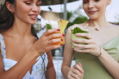 Zarif elbiseli genç kadınlar, kokteyllerin tadını çıkarıyorlar, bardakları tokuşturuyorlar, yaz akşamları modern atmosferik barda, restoranda buluşuyorlar. Arkadaşlık kavramı, parti, eğlence, kutlama, rahatlama.