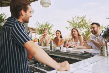 Gençler, arkadaşlar modern barda buluşuyor, açık hava restoranı, kokteyllerin ve erkek barmenle konuşmanın tadını çıkarıyor. Arkadaşlık kavramı, parti, eğlence, kutlama, rahatlama.