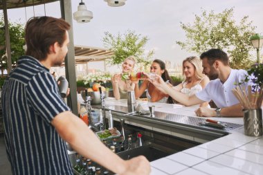 Gençler, arkadaşlar modern barda buluşuyor, açık hava restoranı, kokteyllerin ve erkek barmenle konuşmanın tadını çıkarıyor. Arkadaşlık kavramı, parti, eğlence, kutlama, rahatlama.