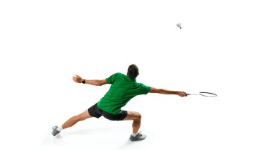 Güç ve çeviklik. Genç bir adam, yeşil tişörtlü badminton atleti, antrenman yapıyor, oynuyor, beyaz arka planda izole edilmiş raketle servis aletine vuruyor. Spor anlayışı, rekabet, aktif yaşam tarzı