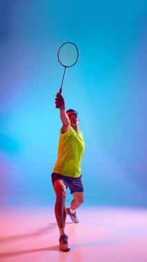 Odaklanmış bir adamın, badminton oyuncusunun raketle mekiğe vuruşunun, neon rengi pembe arka planda gradyan çalışmasının tam boy görüntüsü. Spor anlayışı, rekabet, aktif yaşam tarzı