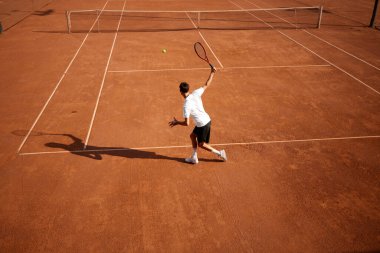 Genç bir adamın en iyi görüntüsü, kil sahada hareket eden bir tenisçi, tenis oynuyor, forehand vuruş çalışması yapıyor. Dinamik ve odaklanma. Spor anlayışı, rekabet, aktif ve sağlıklı yaşam tarzı